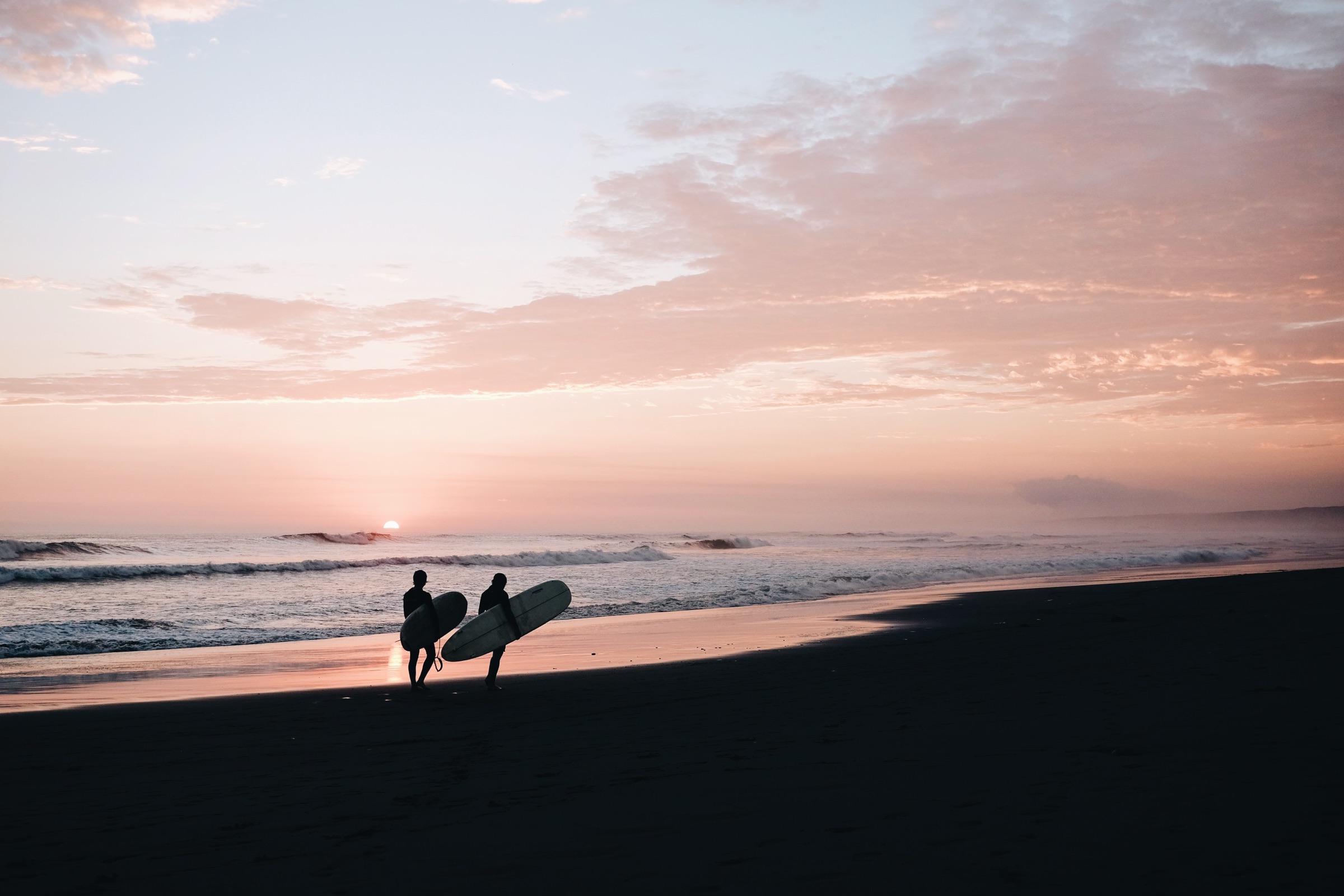 Two surfers walking the beach at dusk
